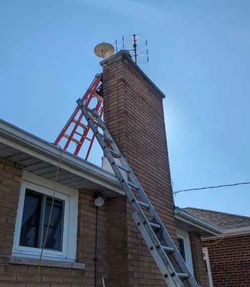 Tall brick chimney on a bungalow with ladders up the side and an old TV antenna on top